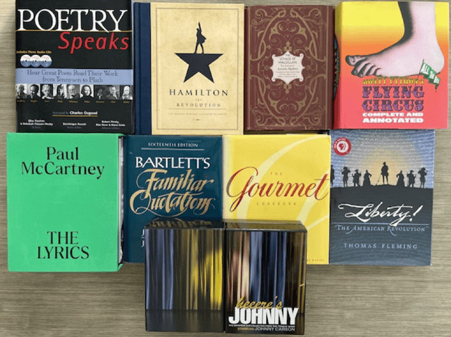 Friends' book auction table. Titles include: Poetry Speaks, Hamilton the Revolution, The Voyage of Magellan, Monty Python's Flying Circus Complete and Annotated, Paul McCartney the Lyrics, Bartlett's Familiar Quotations, The Gourmet Cookbook, Liberty! The American Revolution, and Heeeere's Johnny.